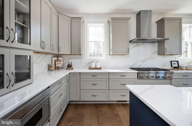 kitchen featuring stainless steel appliances, dark hardwood / wood-style floors, gray cabinets, decorative backsplash, and wall chimney exhaust hood