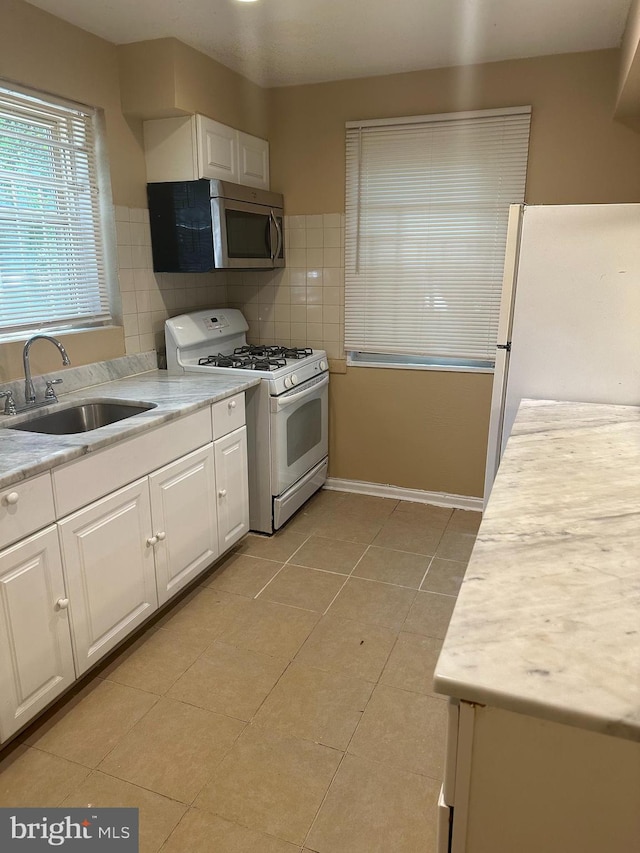 kitchen featuring sink, light tile patterned floors, white appliances, decorative backsplash, and white cabinets