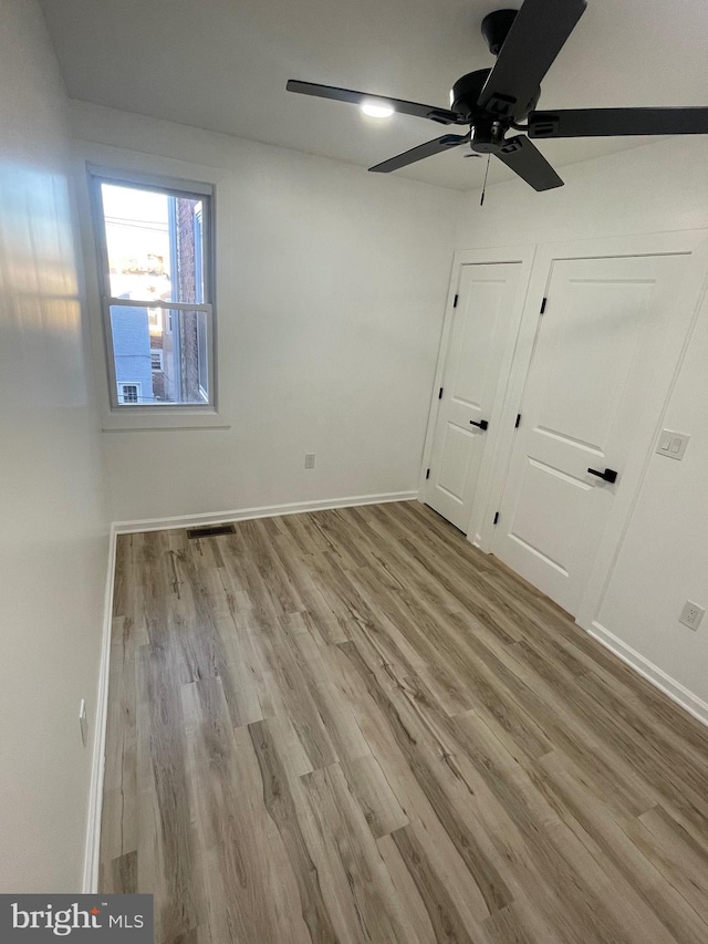 unfurnished bedroom with light hardwood / wood-style floors, two closets, and ceiling fan