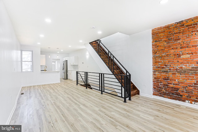 unfurnished living room with brick wall, sink, and light wood-type flooring