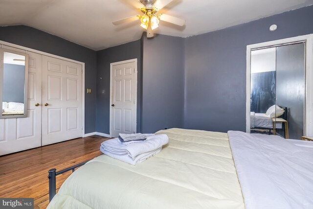 bedroom featuring vaulted ceiling, two closets, hardwood / wood-style flooring, and ceiling fan