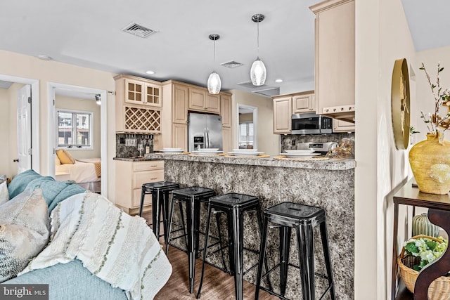 kitchen with hanging light fixtures, kitchen peninsula, hardwood / wood-style floors, appliances with stainless steel finishes, and tasteful backsplash