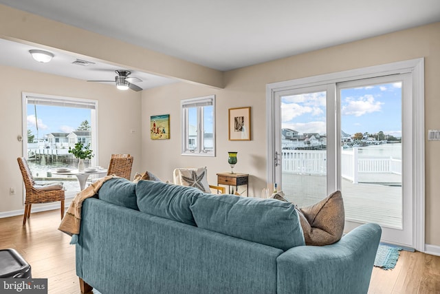 living room with light hardwood / wood-style flooring, a water view, a healthy amount of sunlight, and ceiling fan