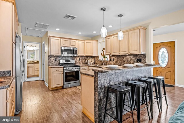 kitchen with backsplash, appliances with stainless steel finishes, a kitchen breakfast bar, light wood-type flooring, and sink