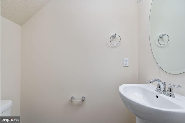 bathroom featuring toilet, a textured ceiling, and sink