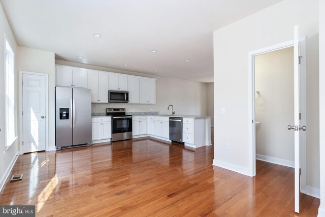 kitchen with appliances with stainless steel finishes, white cabinets, sink, and light wood-type flooring