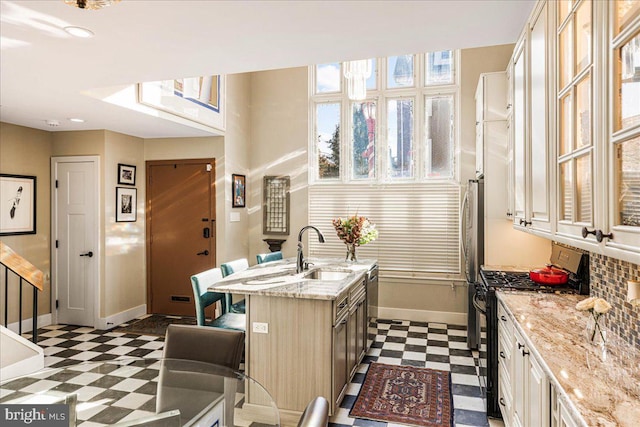 kitchen featuring a center island with sink, light stone counters, sink, a kitchen breakfast bar, and appliances with stainless steel finishes