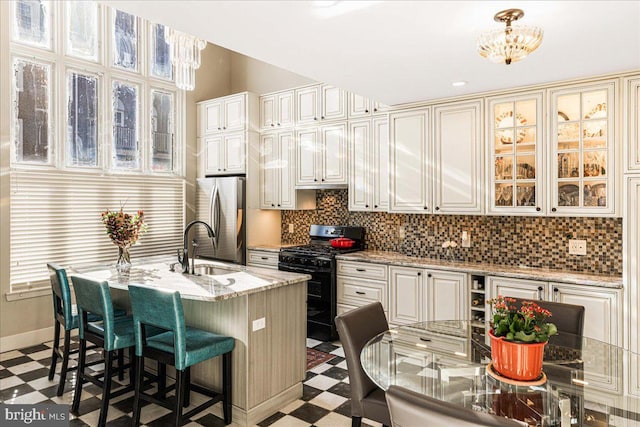 kitchen featuring stainless steel fridge, black range with gas stovetop, pendant lighting, sink, and a kitchen island with sink