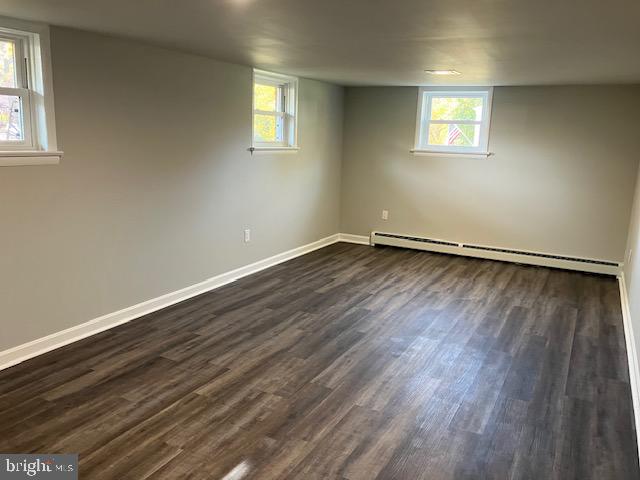 basement featuring dark hardwood / wood-style flooring, a baseboard radiator, and a wealth of natural light