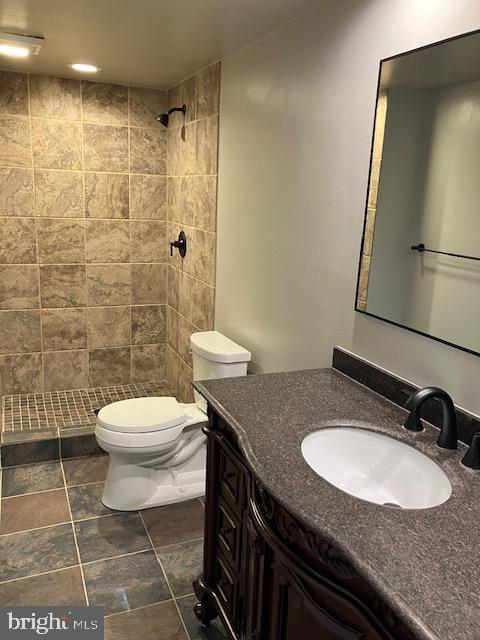 bathroom featuring vanity, tiled shower, and toilet