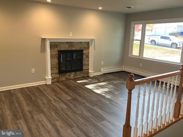 unfurnished living room featuring baseboard heating, a fireplace, and dark hardwood / wood-style flooring