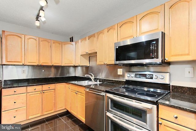 kitchen with sink, appliances with stainless steel finishes, light brown cabinets, dark stone countertops, and rail lighting