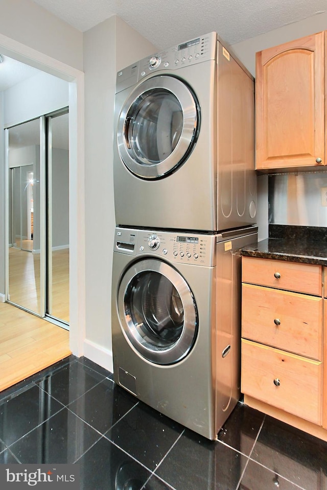 laundry room with cabinets, dark tile patterned floors, and stacked washer / dryer