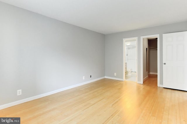 unfurnished bedroom featuring a closet, a spacious closet, hardwood / wood-style flooring, and ensuite bath