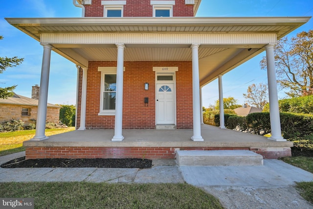 view of exterior entry with a porch and brick siding