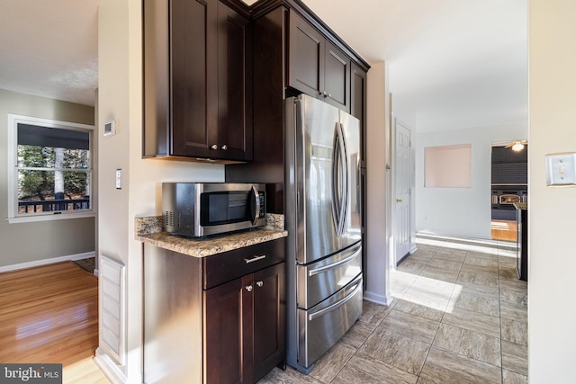 kitchen with light stone countertops, dark brown cabinets, stainless steel appliances, and light hardwood / wood-style floors