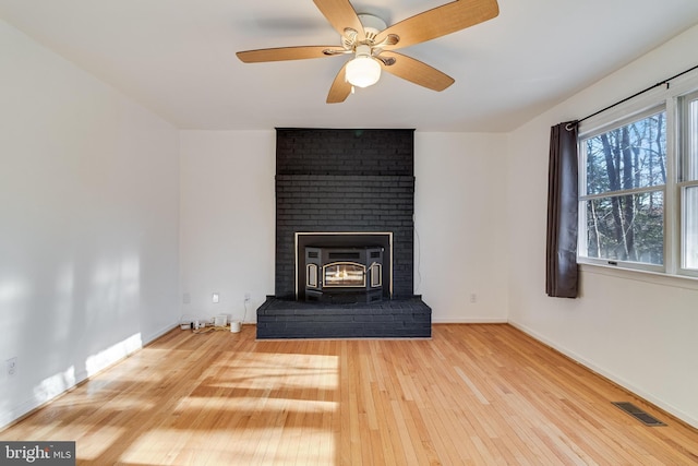 unfurnished living room with light hardwood / wood-style floors, a wood stove, and ceiling fan