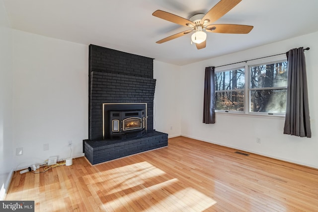 unfurnished living room with hardwood / wood-style flooring, ceiling fan, and a wood stove