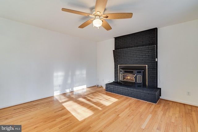 unfurnished living room with hardwood / wood-style floors, a wood stove, and ceiling fan