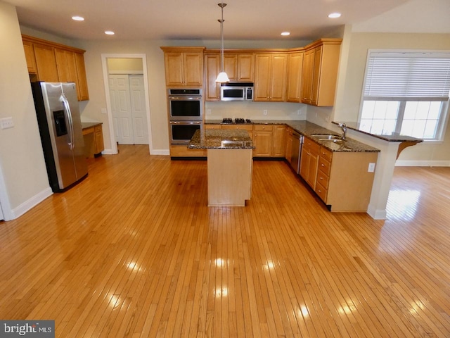 kitchen with appliances with stainless steel finishes, pendant lighting, light hardwood / wood-style floors, a breakfast bar, and a center island