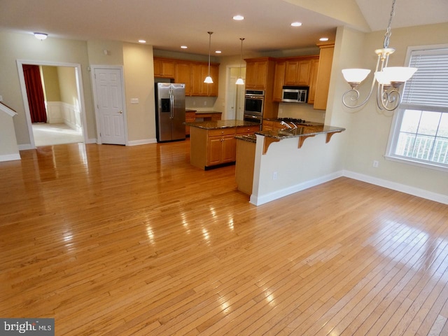 kitchen featuring kitchen peninsula, appliances with stainless steel finishes, a breakfast bar area, hanging light fixtures, and light wood-type flooring