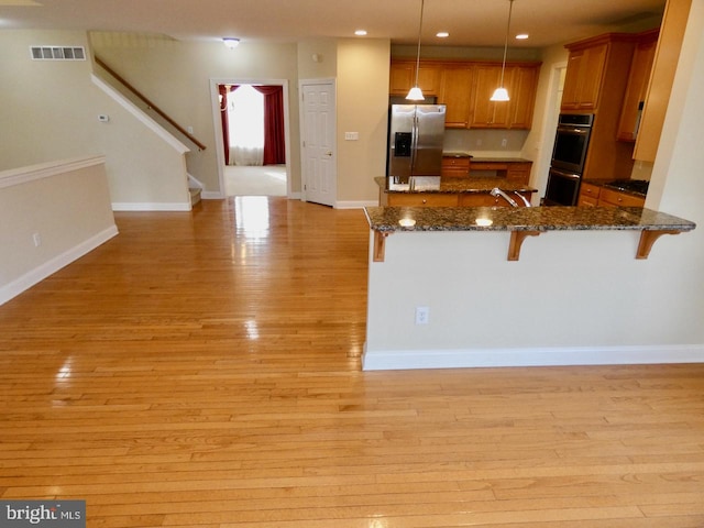 kitchen featuring stainless steel appliances, dark stone counters, pendant lighting, light hardwood / wood-style floors, and a breakfast bar area