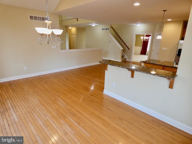 kitchen with kitchen peninsula, light hardwood / wood-style floors, hanging light fixtures, and a notable chandelier