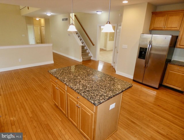 kitchen featuring light wood-type flooring, hanging light fixtures, dark stone counters, and stainless steel fridge