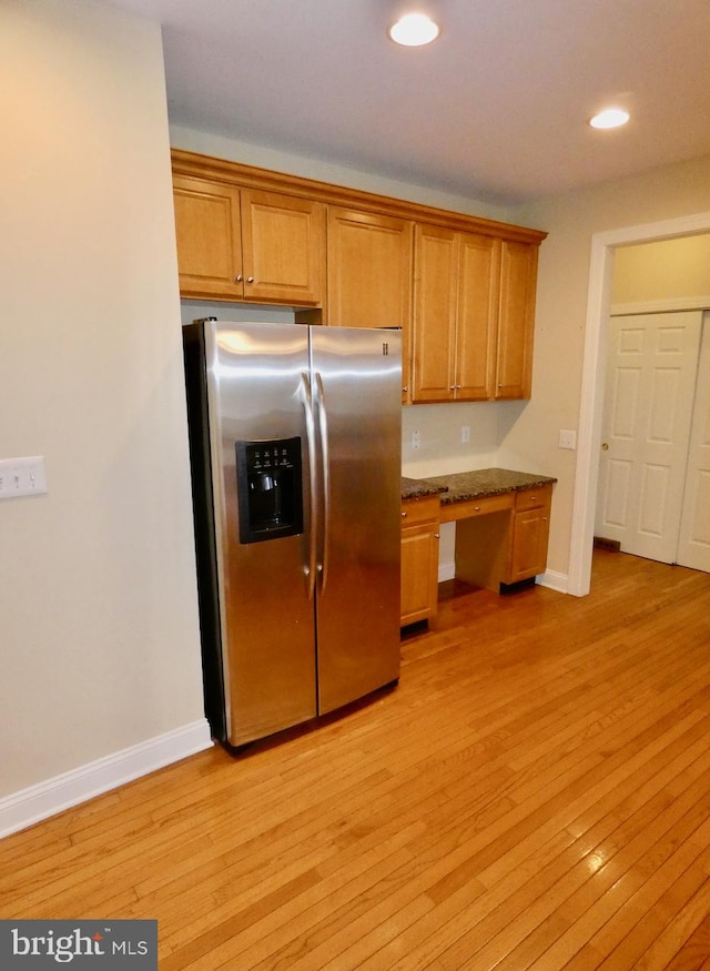 kitchen with built in desk, stainless steel fridge with ice dispenser, dark stone countertops, and light wood-type flooring