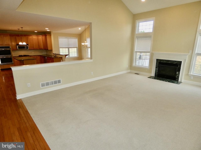 unfurnished living room with a high end fireplace, light hardwood / wood-style flooring, vaulted ceiling, and a notable chandelier