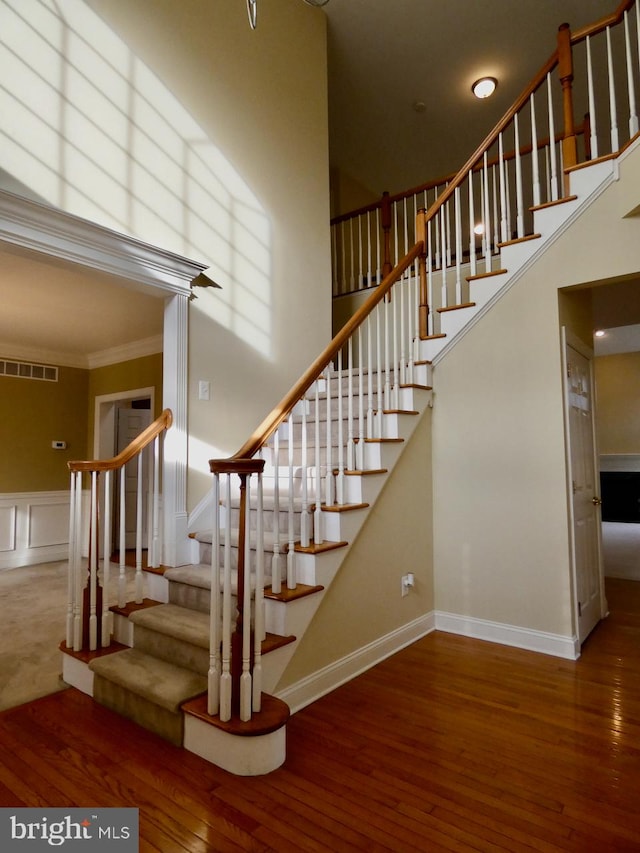 stairs with a high ceiling, wood-type flooring, and crown molding