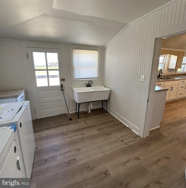 clothes washing area featuring sink, washer and clothes dryer, light wood-type flooring, and wooden walls