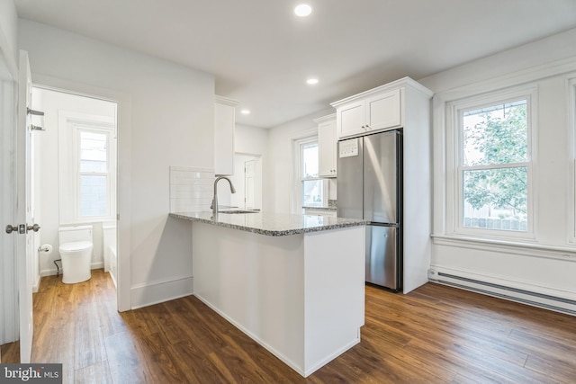 kitchen with kitchen peninsula, stainless steel fridge, white cabinets, and a healthy amount of sunlight