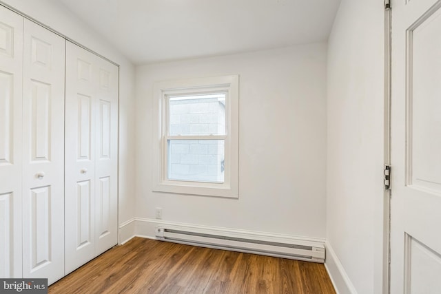 unfurnished bedroom featuring a closet, baseboard heating, and hardwood / wood-style floors