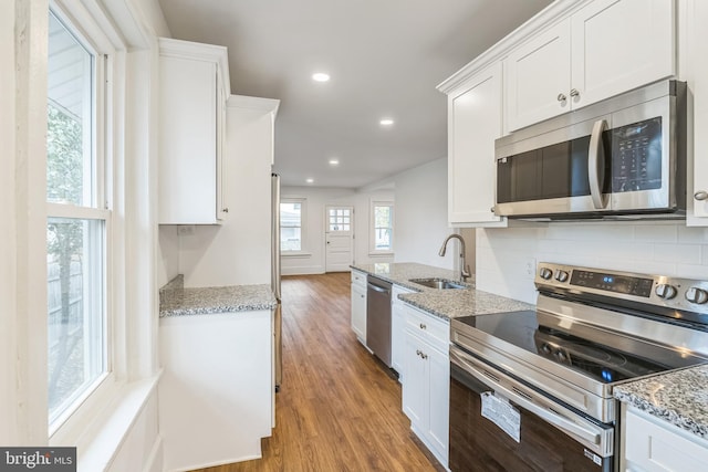 kitchen featuring light stone countertops, appliances with stainless steel finishes, sink, light wood-type flooring, and white cabinets