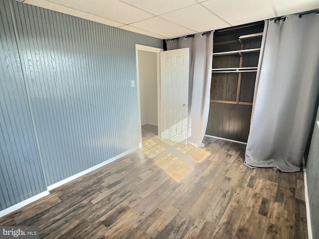 spare room with a paneled ceiling, wooden walls, and wood-type flooring