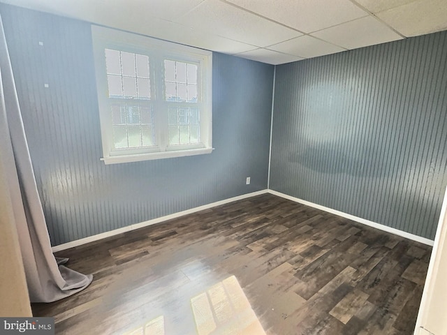 empty room with dark hardwood / wood-style floors, wooden walls, and a drop ceiling