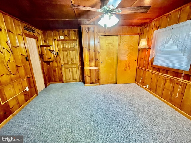 unfurnished room with ceiling fan, wood walls, and carpet