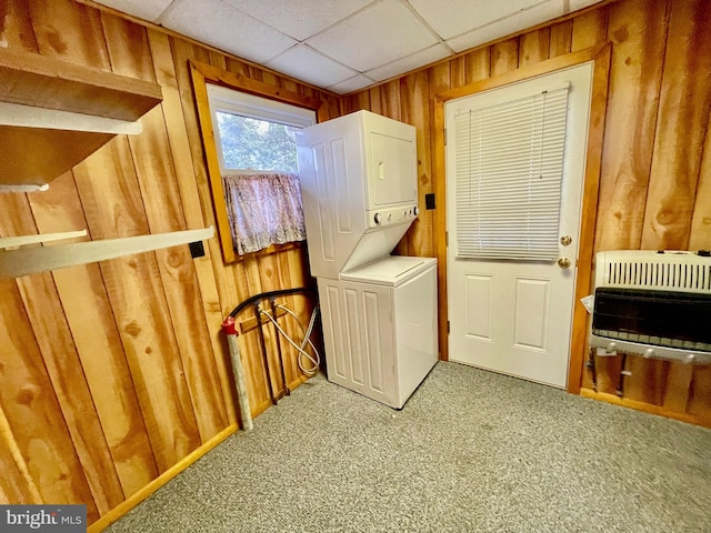 laundry area with wood walls, stacked washing maching and dryer, carpet flooring, and heating unit