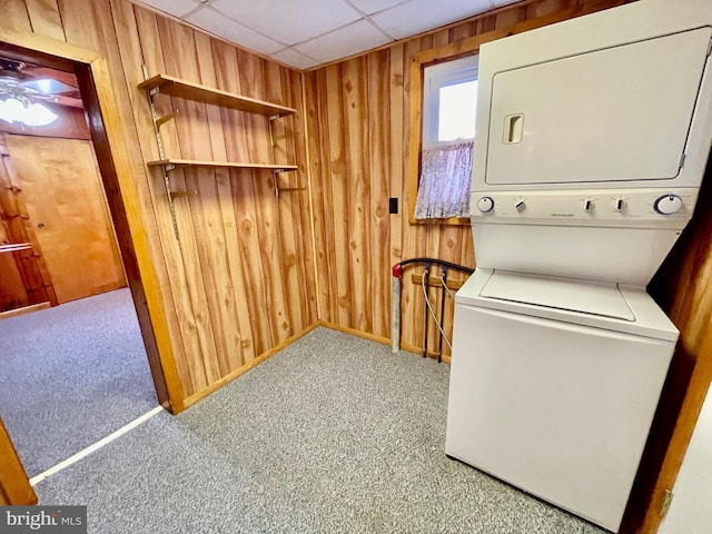 laundry area with wooden walls, stacked washer and dryer, and carpet flooring