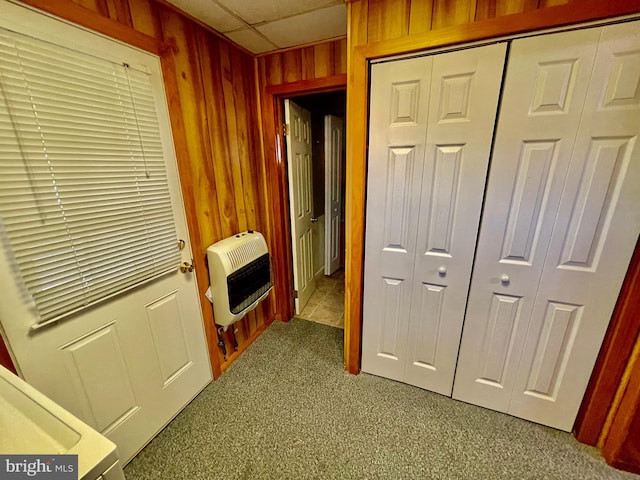 hall featuring carpet, a drop ceiling, heating unit, and wood walls