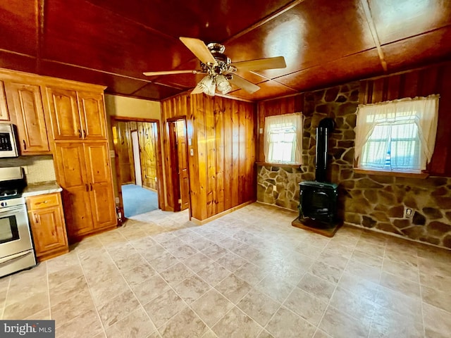 kitchen with white appliances, ceiling fan, wood walls, and a wood stove