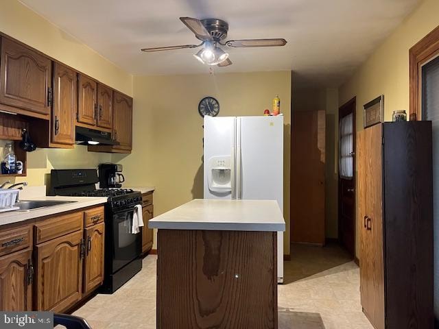 kitchen featuring sink, black gas range oven, ceiling fan, white refrigerator with ice dispenser, and a kitchen island