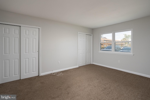 unfurnished bedroom with dark colored carpet and two closets