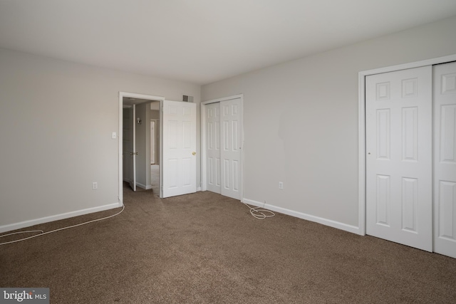 unfurnished bedroom featuring multiple closets and dark colored carpet