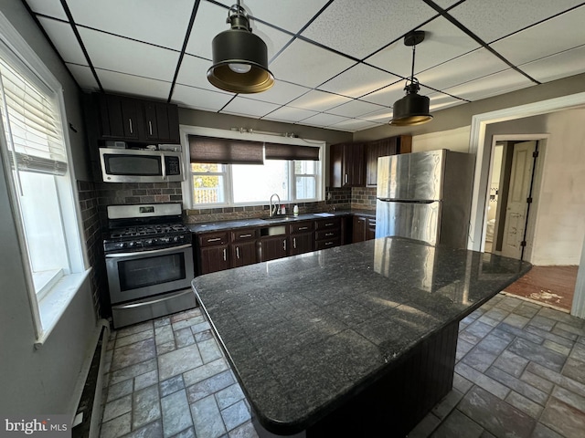 kitchen featuring a paneled ceiling, stainless steel appliances, decorative backsplash, and hanging light fixtures