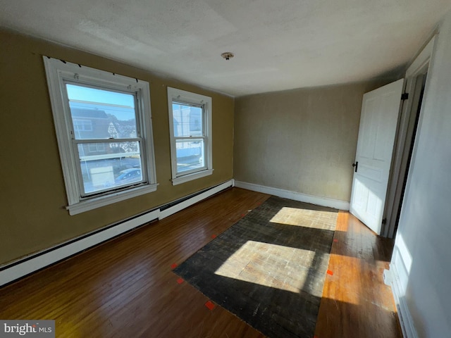 unfurnished room with baseboard heating and dark hardwood / wood-style flooring