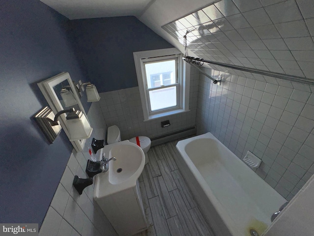 bathroom featuring a baseboard heating unit, tile walls, vaulted ceiling, toilet, and sink