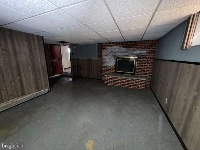 basement featuring a paneled ceiling, a brick fireplace, and wooden walls