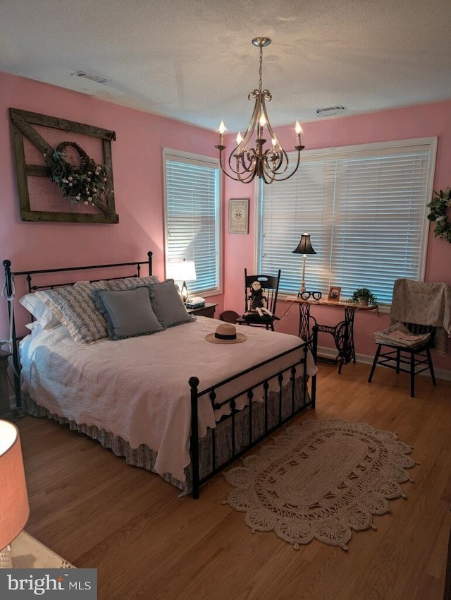 bedroom featuring a textured ceiling, wood-type flooring, and an inviting chandelier